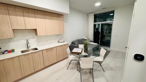 Una cocina moderna con armarios de madera, encimera blanca y un comedor con mesa de vidrio y sillas blancas.