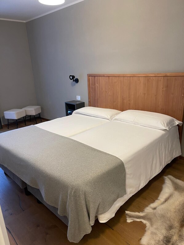 Une chambre à coucher avec un grand lit, une tête de lit en bois, une table de chevet et un petit coin salon avec deux fauteuils.