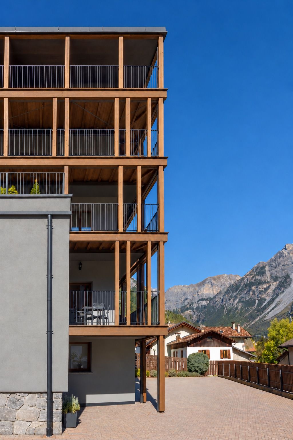 A multi-story building with balconies, a stone facade, and a mountainous backdrop.