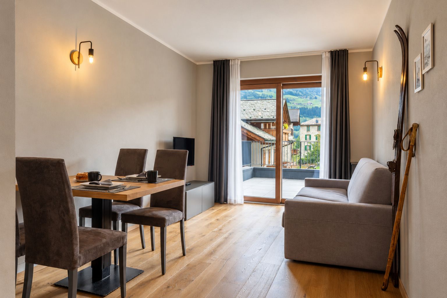 A modern living room with a dining area, a sofa, and a view of a mountainous landscape through large windows.