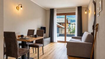 A modern living room with a dining area, a sofa, and a view of a mountainous landscape through large windows.