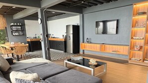 Un salon moderne avec un grand canapé d’angle gris, une table basse en bois et un téléviseur fixé au mur.