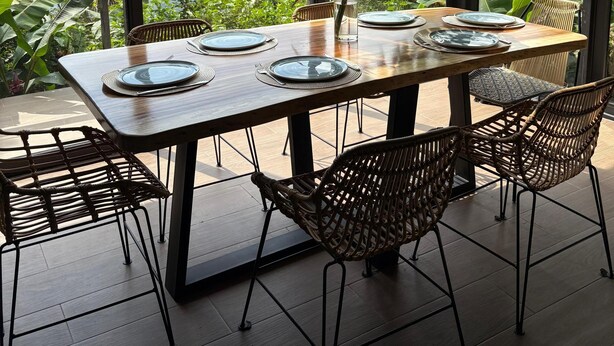 Un coin repas avec une table en bois dressée pour quatre personnes, entourée de chaises en osier, sous un luminaire suspendu.