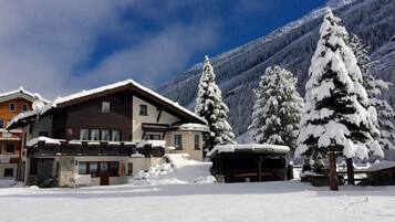 Un edificio cubierto de nieve con un balcón, rodeado de árboles y montañas cargadas de nieve.