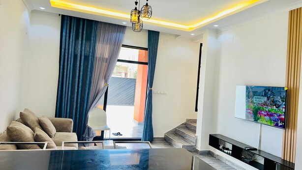 A modern living room with a glass-top coffee table, a sofa, and a TV mounted on the wall.