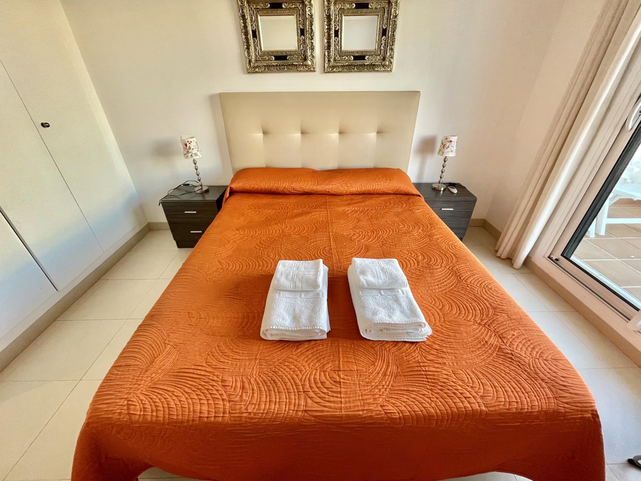 Habitación de hotel con una cama grande, dos mesitas de noche, un cabecero y dos marcos de cuadros colgados en la pared.