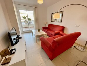 A modern living room with a red sofa, a white coffee table, and a TV on a stand.