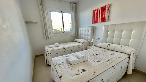 A bedroom with two beds, a window with curtains, a headboard, and a wall-mounted artwork. - Central apartment next to the Balcón de Europa (Nerja)