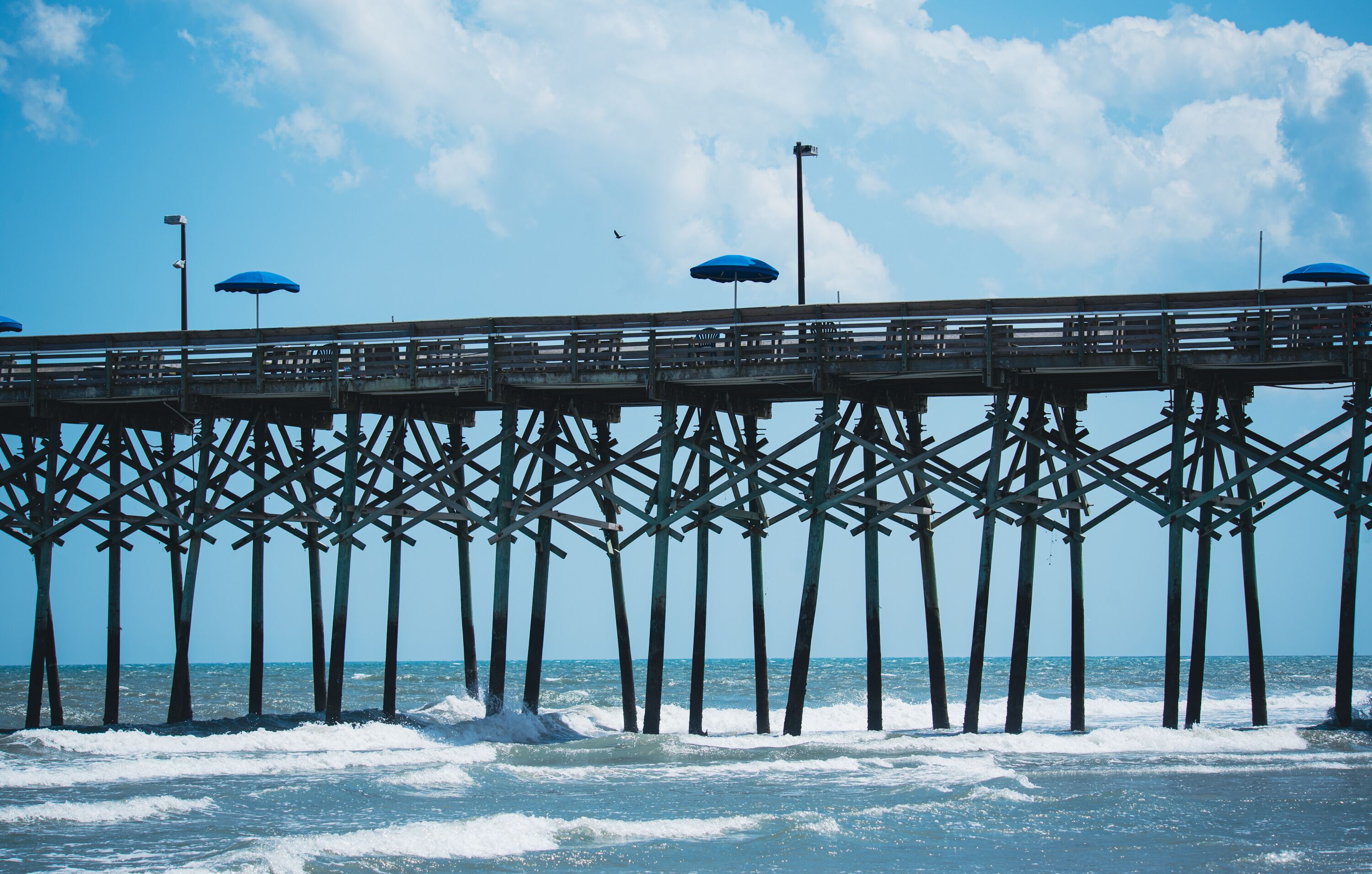 A pier with multiple blue umbrellas and a wooden walkway over the water.