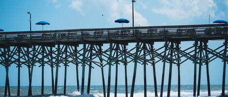 A pier with multiple blue umbrellas and a wooden walkway over the water.