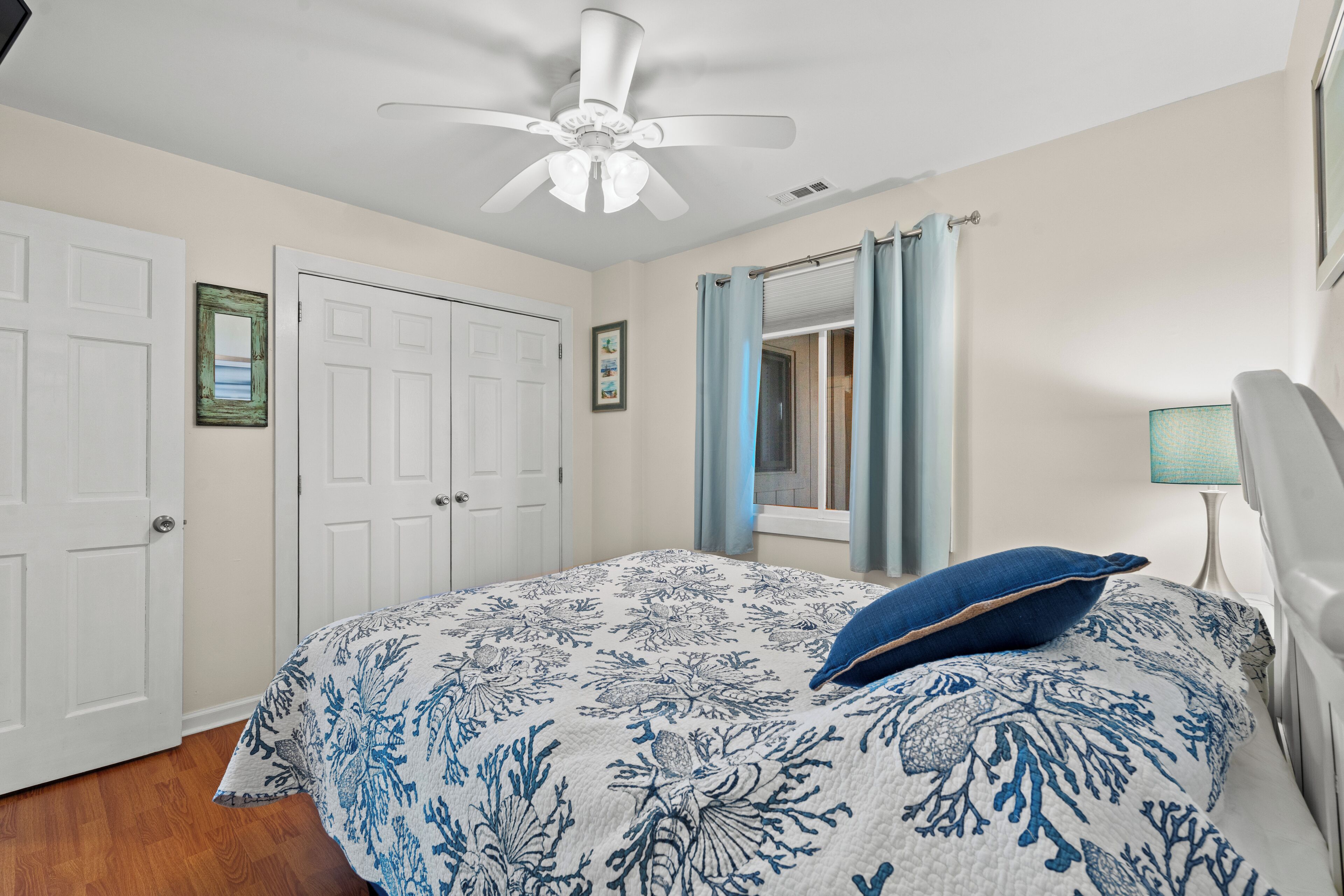 A bedroom with a bed, a ceiling fan, a window with curtains, and a door.