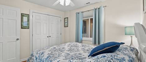A bedroom with a bed, a ceiling fan, a window with curtains, and a door.