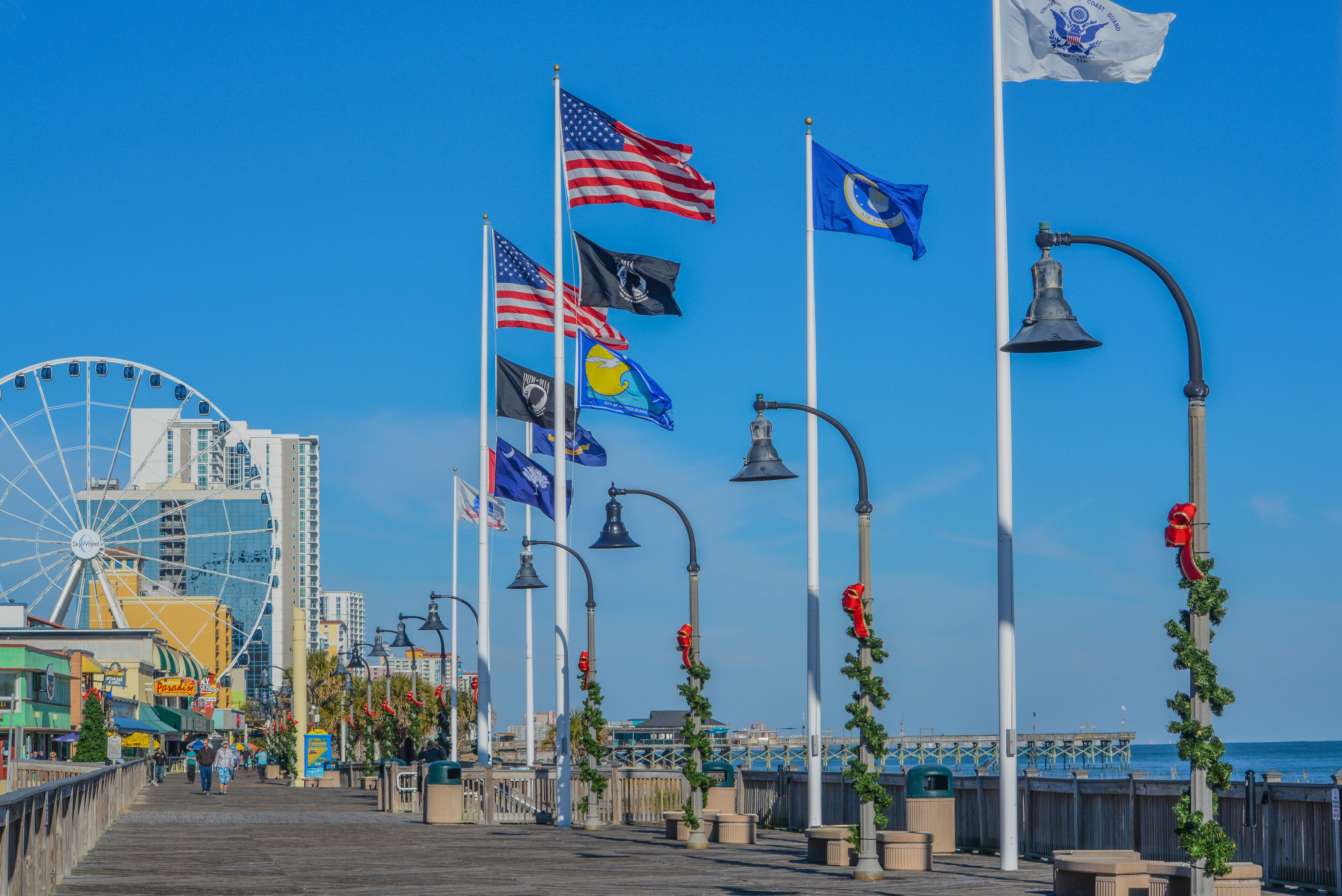 A boardwalk with flags, street lamps, and a Ferris wheel in the background.