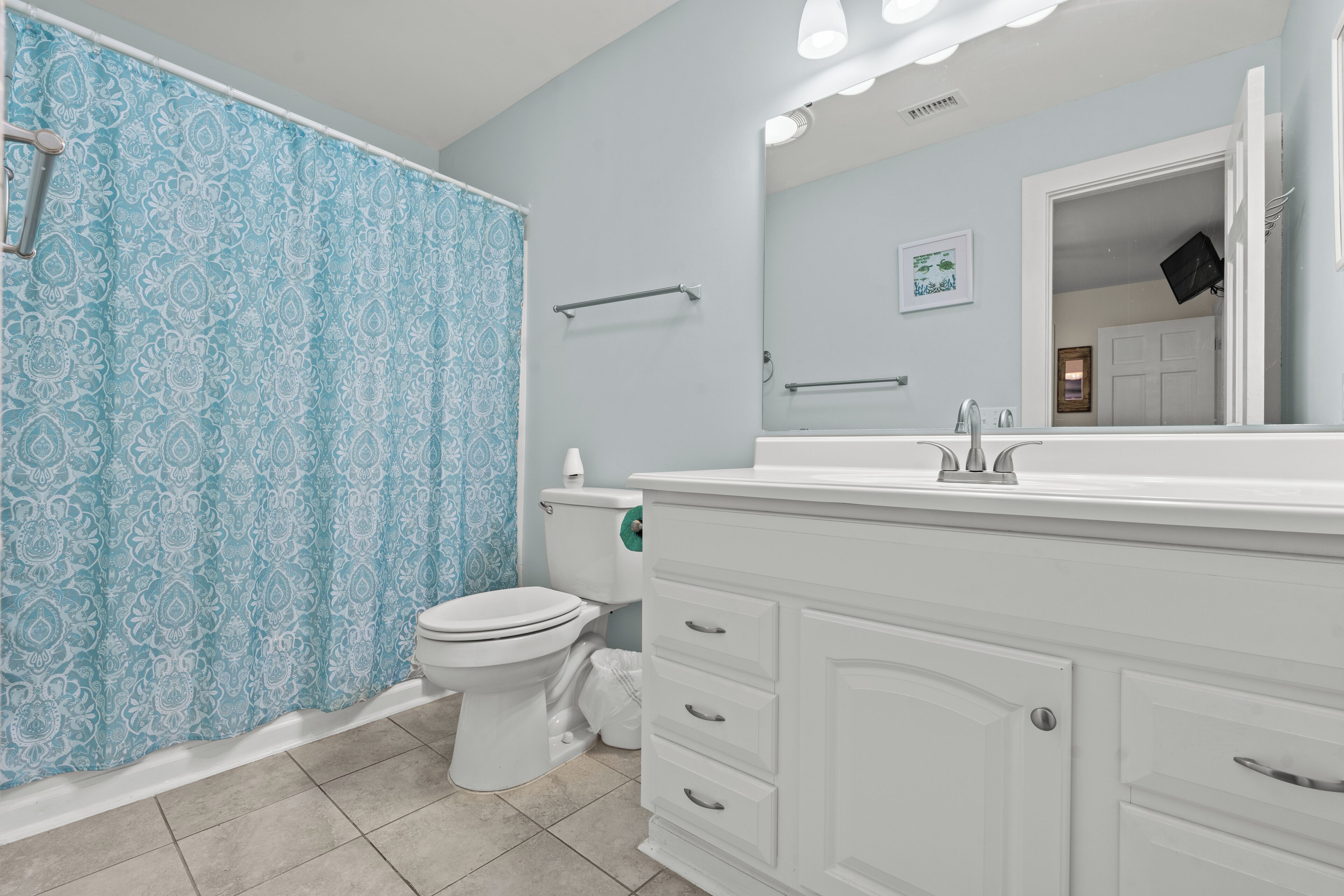 Baño con tocador blanco, inodoro, cortina de ducha y espejo.