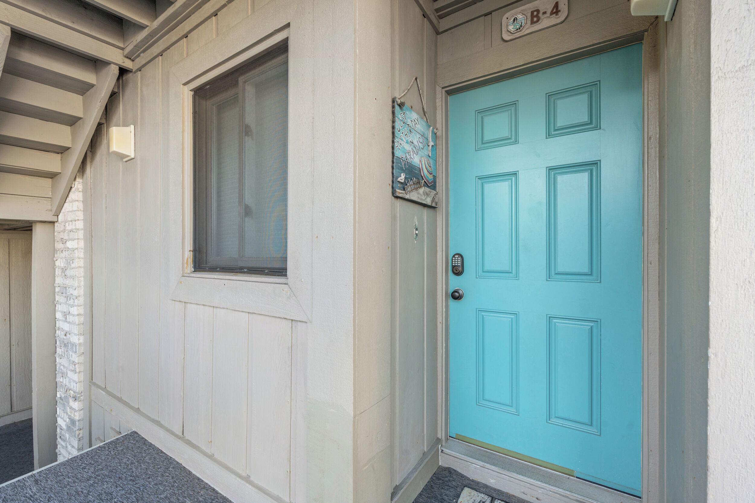 A turquoise door with a small window above it, a mailbox, and a number plate 'B-4'.