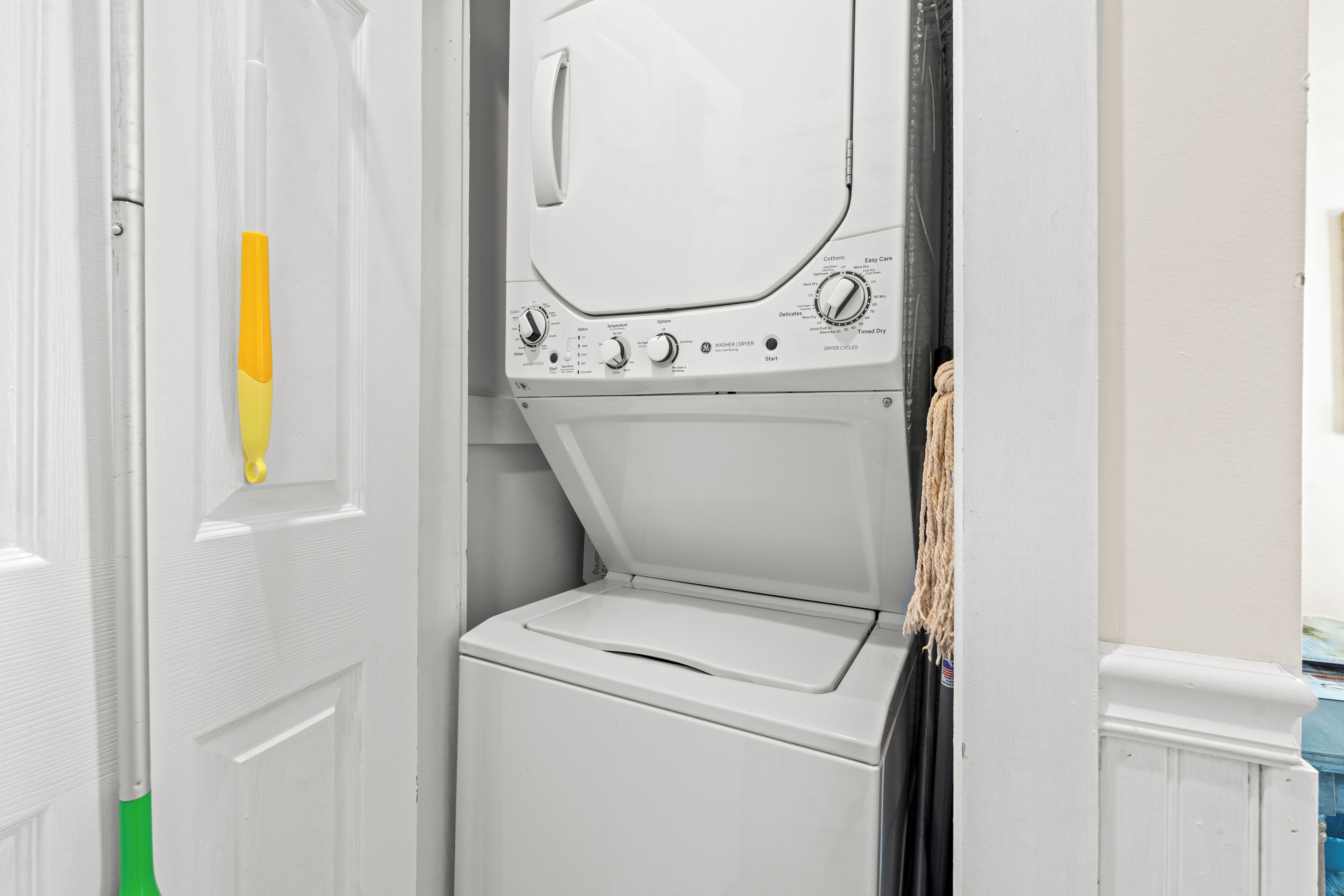 A laundry room with a front-loading washer and dryer, a door with a yellow and white object, and a towel hanging on the wall.