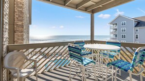 Ein Balkon mit Meerblick, einem runden Tisch und blau-weiß gestreiften Stühlen.