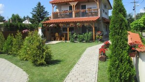 A two-story house with a red-tiled roof, a balcony, and a paved driveway. - Riviera Apartment Family Apartments near the swimming pool and aquapark! (Hajdúszoboszló)