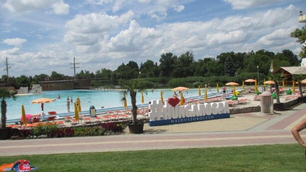 A swimming pool area with lounge chairs and umbrellas, surrounded by greenery and a clear sky. - Riviera Apartment Family Apartments near the swimming pool and aquapark! (Hajdúszoboszló)