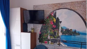 A bedroom with a bed, a TV, a chair, a small table with a bottle, and a mural of a landscape. - Riviera Apartment Family Apartments near the swimming pool and aquapark! (Hajdúszoboszló)