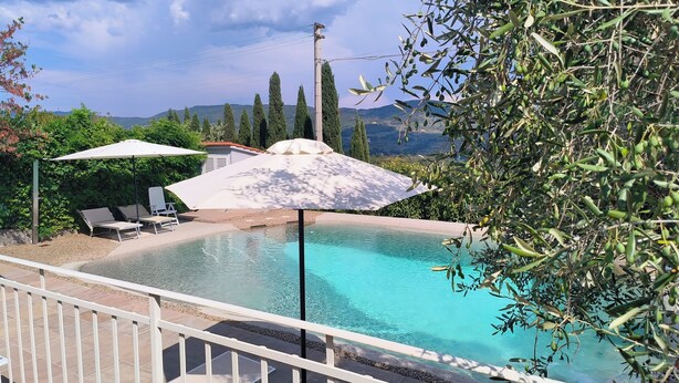 A swimming pool with clear water, surrounded by a deck with lounge chairs and umbrellas, and a view of mountains in the background. - Villa le statue is 5 km from the center of Florence, pool and private parking (Firenze)