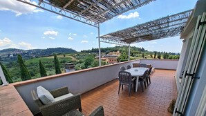A terrace with wicker furniture, a table, and chairs, overlooking a scenic landscape with hills and trees. - Villa le statue is 5 km from the center of Florence, pool and private parking (Firenze)