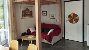 Une pièce avec un lit superposé, un canapé rouge, une petite table avec des livres et un jeu de fléchettes accroché au mur.
