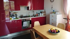Une cuisine avec des placards rouges, une cuisinière et un évier. Il y a une horloge au mur et un panier de fruits sur la table.