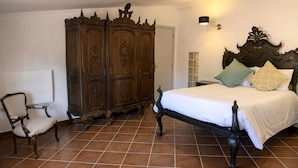 Een slaapkamer met een grote houten garderobe, een bed met een sierlijk hoofdbord en een stoel.