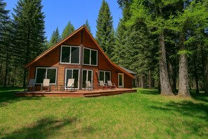 Eine Hütte mit Terrasse und zahlreichen Fenstern, umgeben von hohen Bäumen.