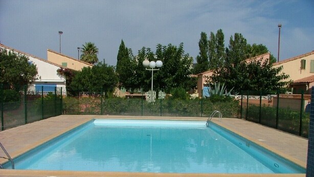 A rectangular swimming pool with a tiled deck, surrounded by a fence and trees. - Coraux Residence house+Veranda park piscines (Canet-en-Roussillon)