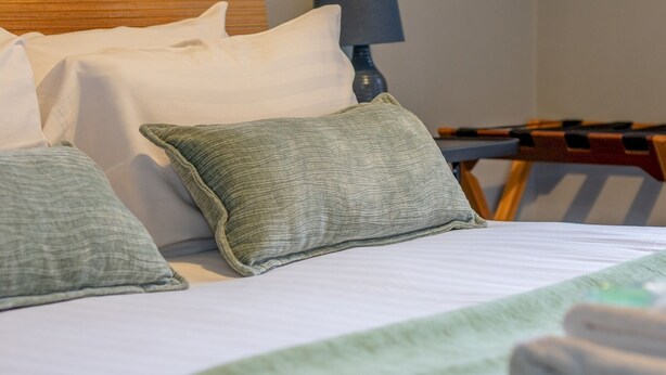 Una cama bien hecha con almohadas blancas y verdes, un cabecero de madera y una lámpara en una mesita de noche.