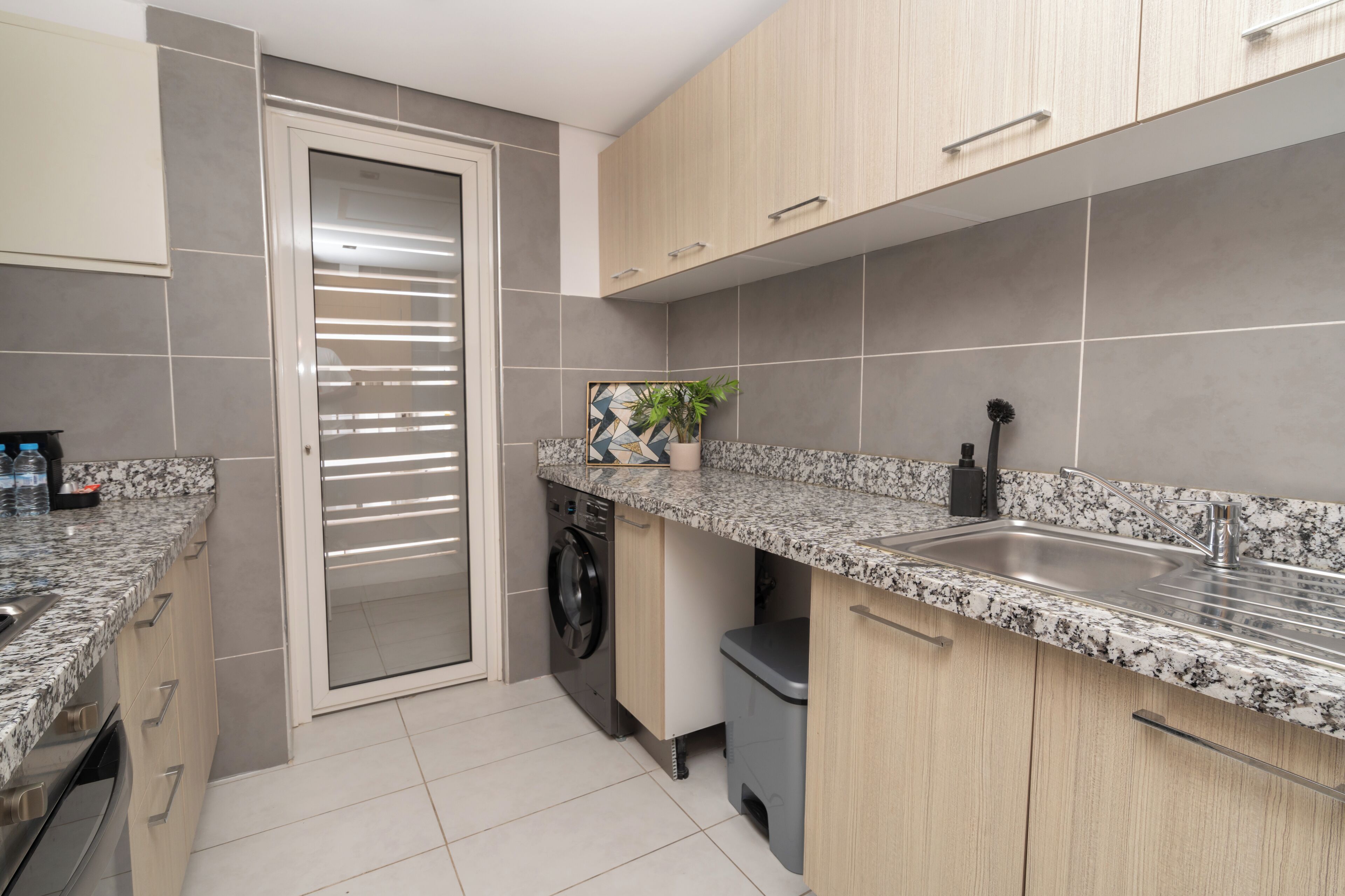 A modern kitchen with granite countertops, a built-in washing machine, and a sink.