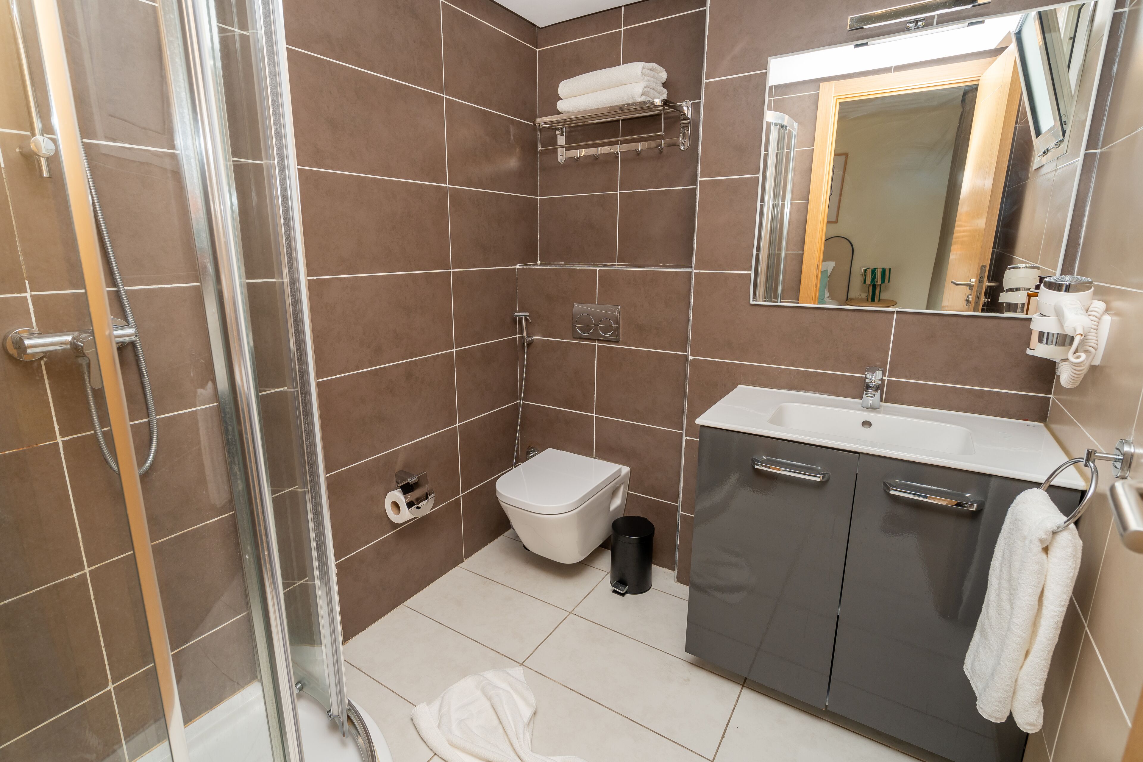 A modern bathroom with a glass-enclosed shower, a toilet, a sink with a mirror, and a towel rack.