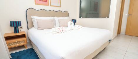 Una cama bien hecha con almohadas, una mesita de noche con una lámpara y un ventanal grande.
