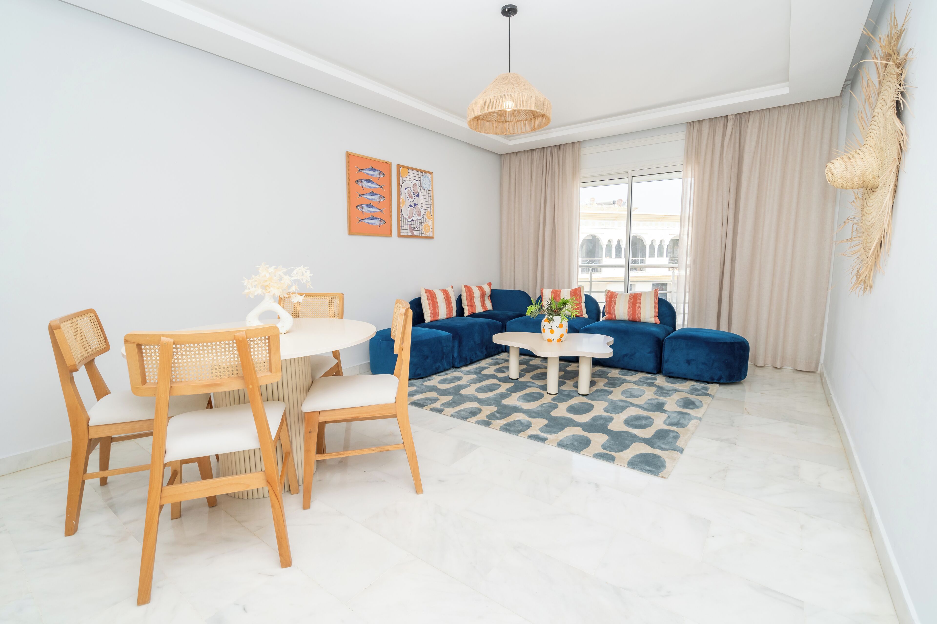 A modern living room with a blue sofa, wooden chairs, a round table, and a hanging light fixture.