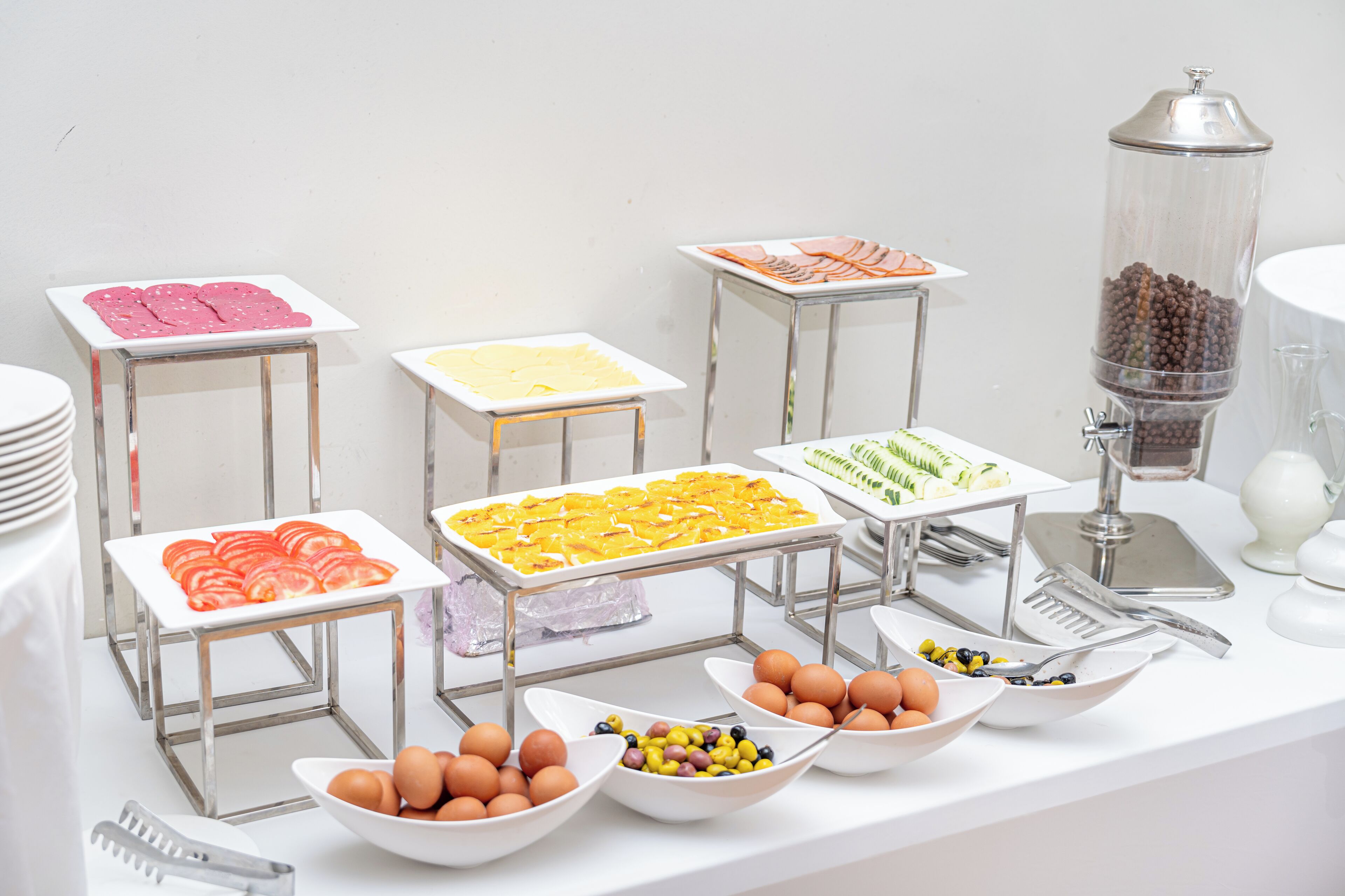 Een buffetopstelling met verschillende soorten eten op schalen en in kommen, waaronder plakjes tomaat, kaas, eieren en een koffieautomaat.