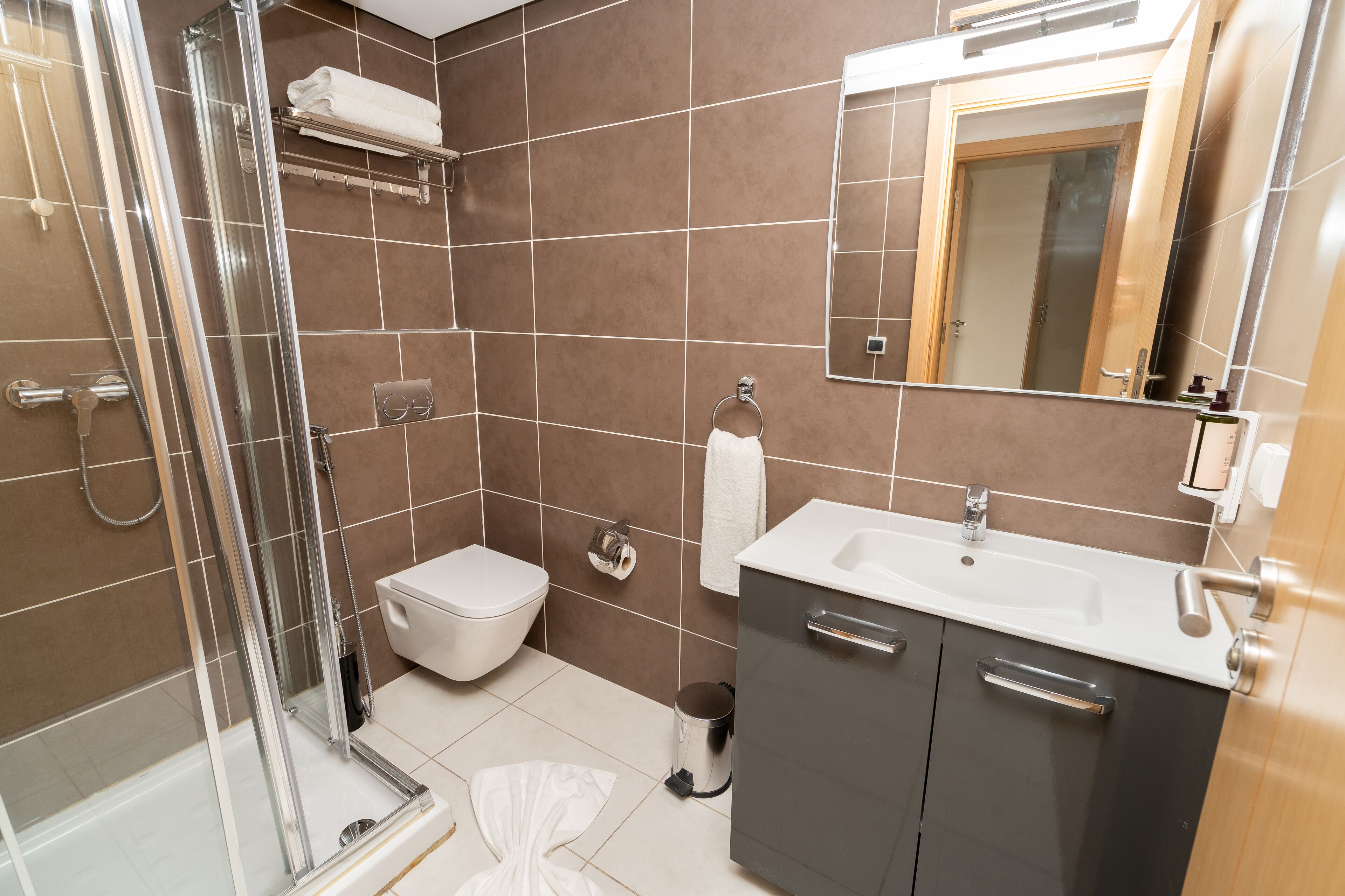 Een moderne badkamer met een douchecabine van glas, een toilet, een wastafel met spiegel en een kast.