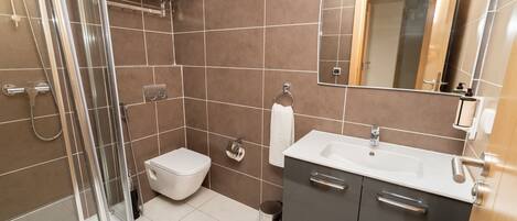 A modern bathroom with a glass shower enclosure, a toilet, a sink with a mirror, and a cabinet.