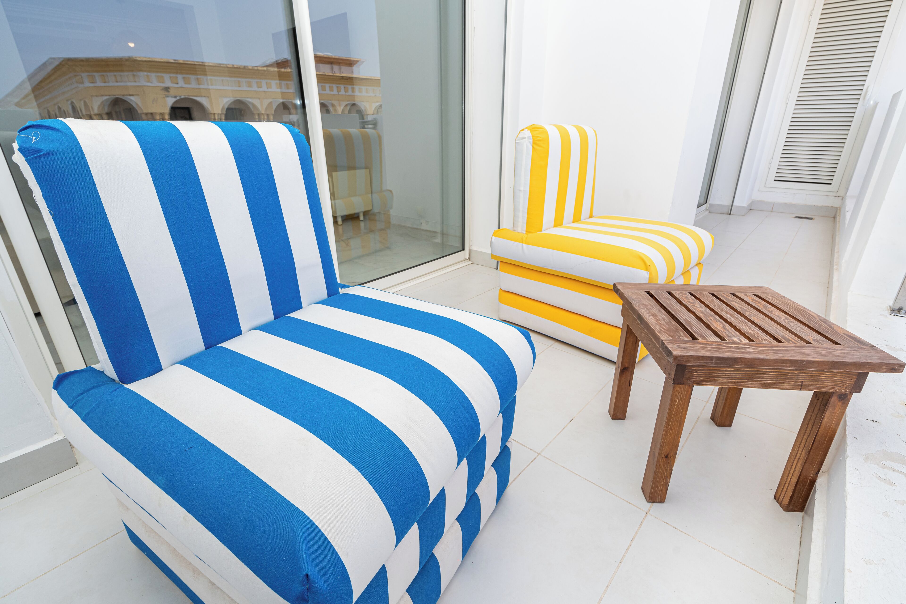 A balcony with a striped blue and white sofa, a yellow and white striped armchair, and a wooden table.