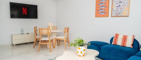 A modern living room with a TV, dining table, chairs, a blue sofa, and artwork on the walls.