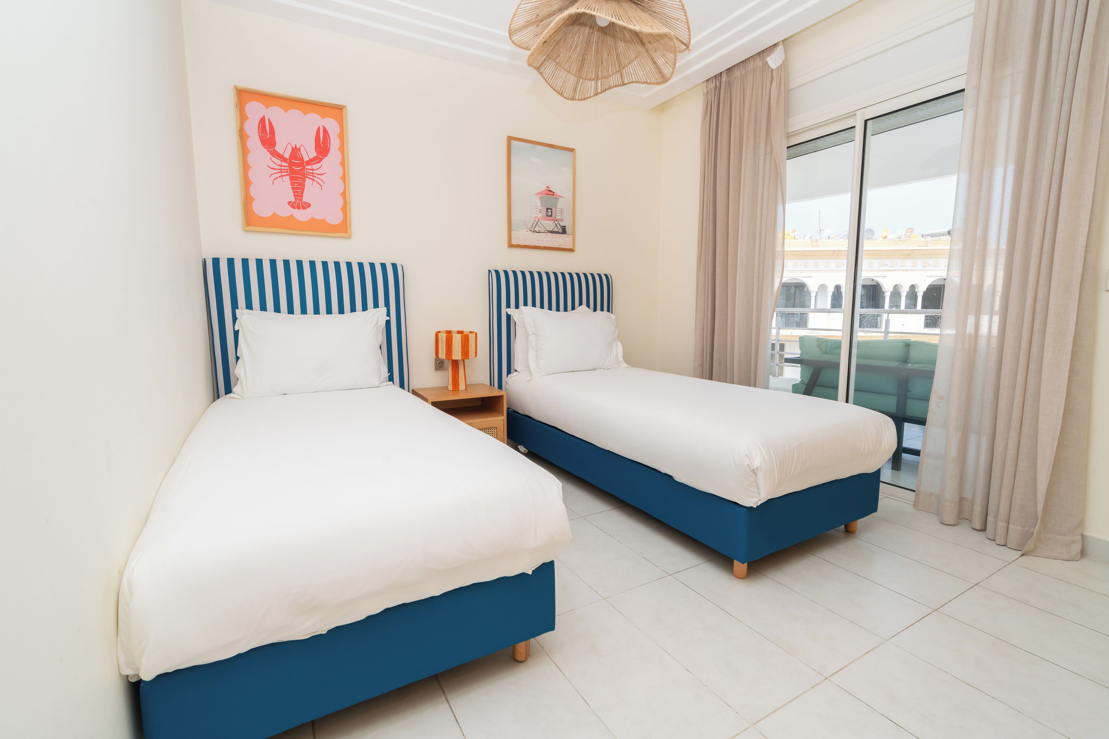 A hotel room with two beds, a balcony with a view, and a framed picture of a lighthouse.