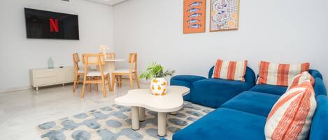 Una sala de estar moderna con un sofá azul, una mesa de centro blanca y un televisor montado en la pared.