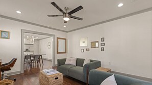 Ein modernes Wohnzimmer mit Deckenventilator, einem Essbereich mit Tisch und Stühlen sowie einer Küche im Hintergrund.
