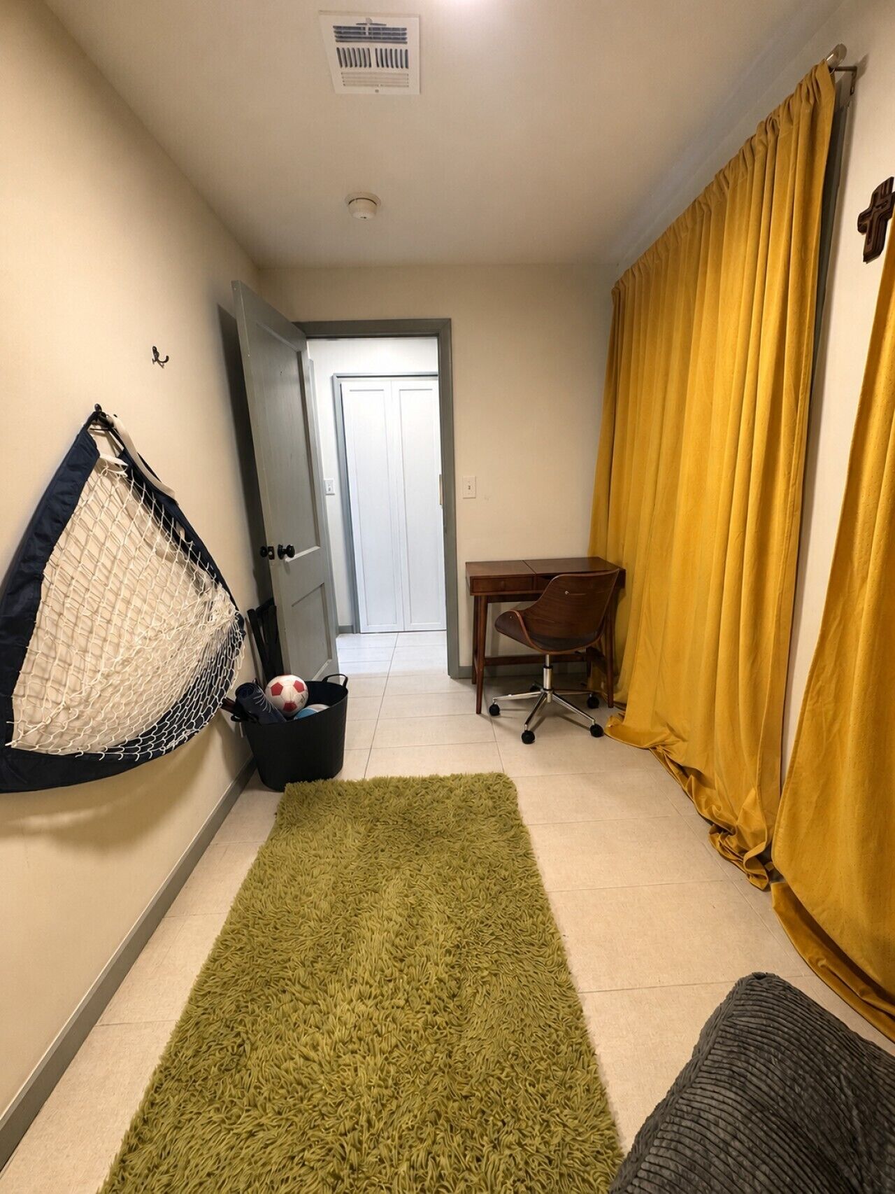 A room with a green rug, a desk, a chair, a hanging net, and a door leading to another room.