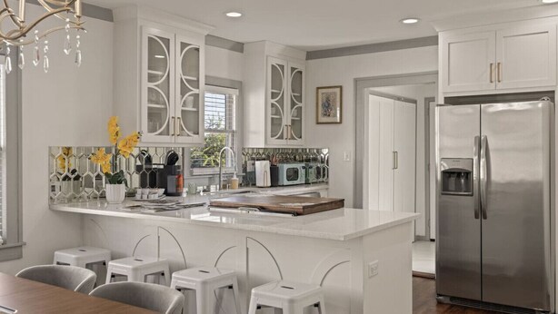 Una cucina moderna con mobili bianchi, un'isola centrale con sgabelli, un frigorifero in acciaio inossidabile e un lampadario.