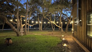 Ein hölzernes Gebäude mit einem Kiesweg, der zu einer Wiese mit Bäumen und Lichterketten führt.