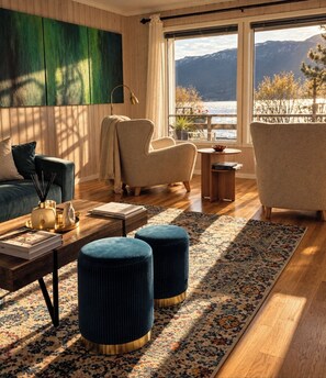 A modern living room with a view of a lake and mountains, featuring a sofa, armchairs, a coffee table, and a patterned rug. - La Casa Senja Seaview Villa with Sauna (Troms)