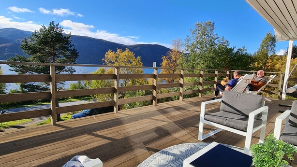 A wooden deck with outdoor seating and a view of mountains and a lake. - La Casa Senja Seaview Villa with Sauna (Troms)