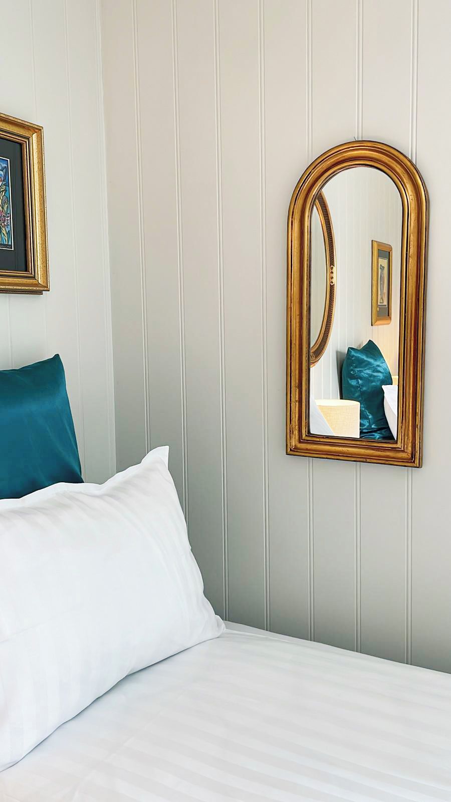 A hotel room with a bed, a large mirror, and a framed picture on the wall.